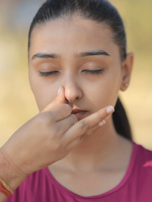 Gros plan sur une jeune femme les yeux fermés pratiquant la respiration alternée, deux doigts posés contre la narine